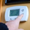 Should I Select On or Auto on My Thermostat? A person lowers temperature on a home thermostat. Enegry saving concept